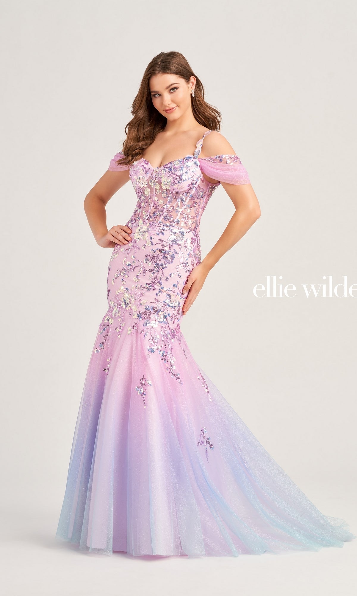 A woman wearing the Cold-Shoulder Ellie Wilde Long Prom Dress EW35056, featuring sequins in pastel pink and purple and a mermaid silhouette, stands against a light background.